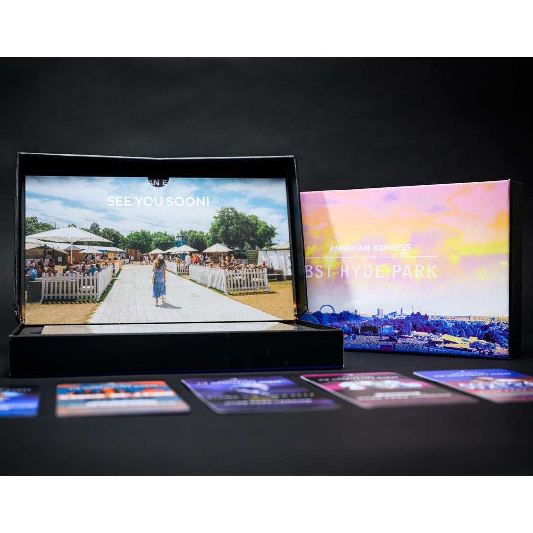 Open CLICK & COLLECT: Bon Jovi VIP Gift Box displaying a photo of a festival pathway, with the box lid featuring a sunset skyline illustration and several souvenir tickets laid out in the foreground.